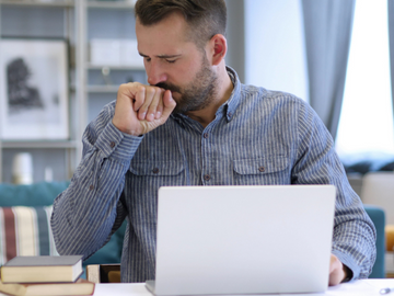 A man coughing infront of his laptop because of smoking